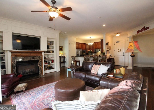 living room with ceiling fan with notable chandelier, ornamental molding, dark wood-type flooring, and a high end fireplace