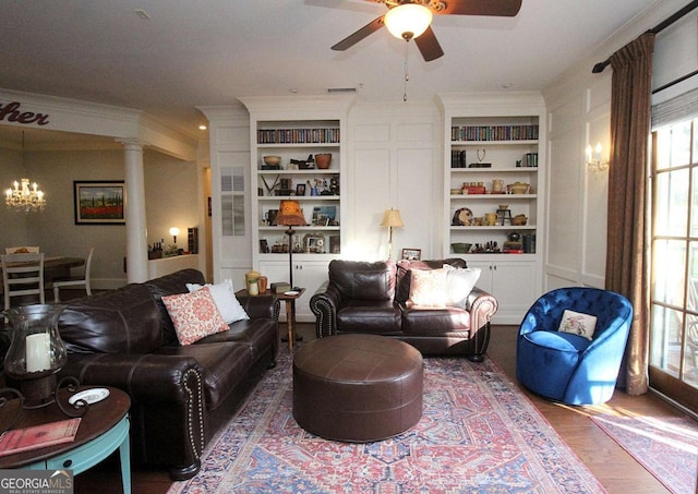 living room with built in shelves, hardwood / wood-style floors, ornate columns, and ceiling fan with notable chandelier