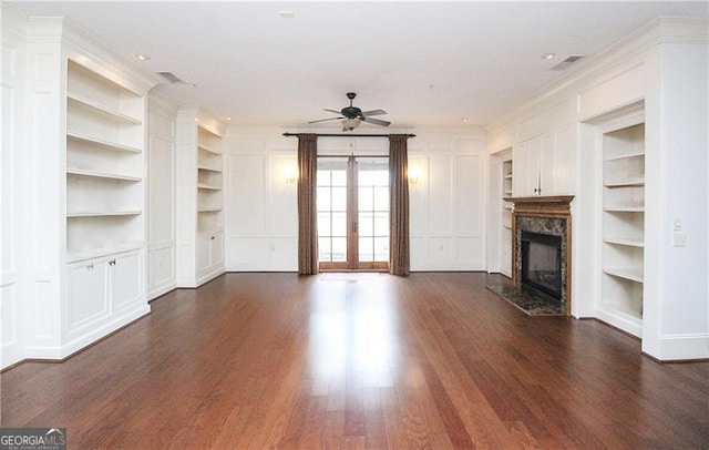 unfurnished living room with built in features, a premium fireplace, dark wood-type flooring, a ceiling fan, and ornamental molding