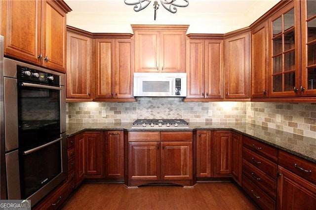 kitchen featuring stainless steel appliances, a chandelier, dark wood-type flooring, dark stone countertops, and tasteful backsplash