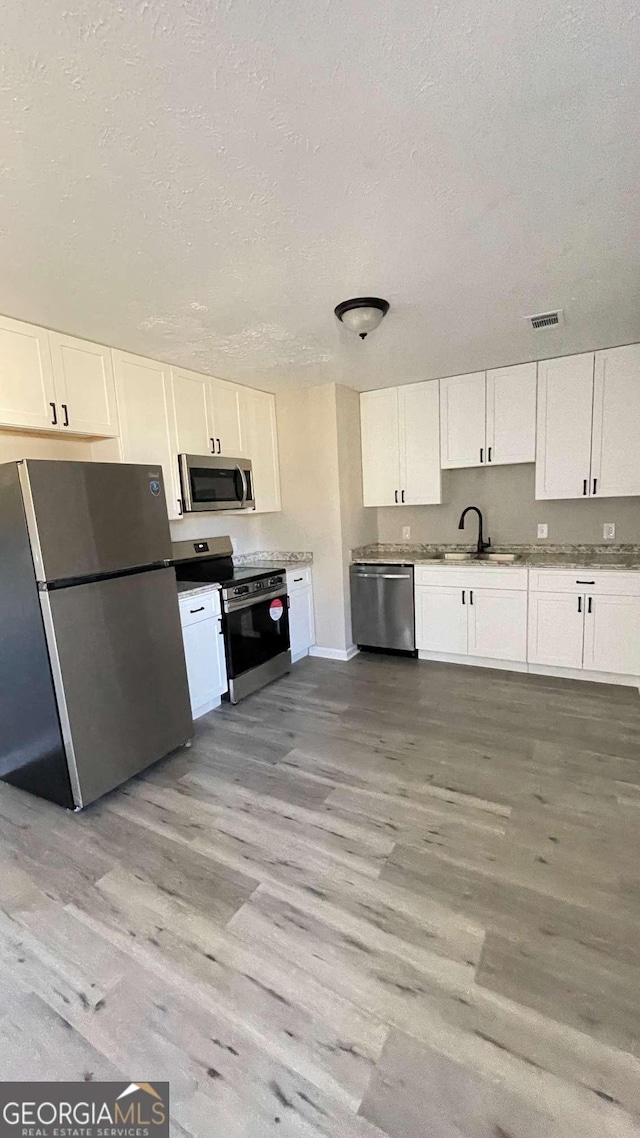 kitchen featuring sink, stainless steel appliances, white cabinetry, and light hardwood / wood-style flooring