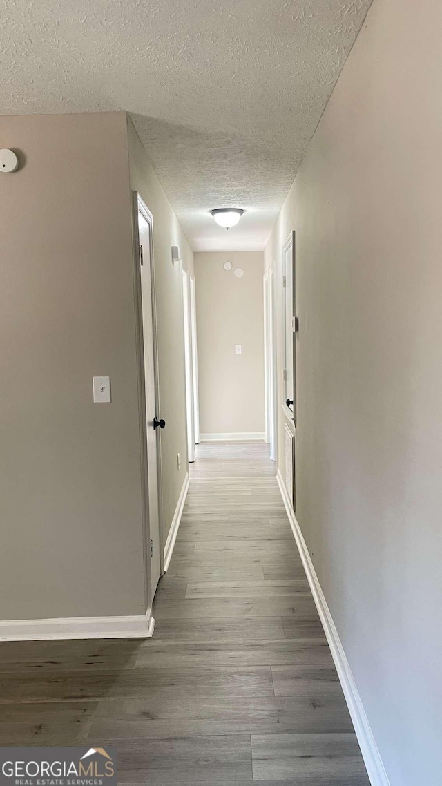 hallway with a textured ceiling and hardwood / wood-style flooring