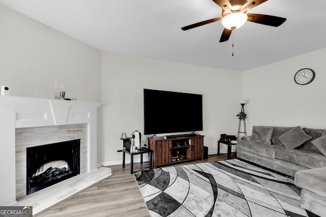 living room with a tile fireplace, light wood-type flooring, and ceiling fan