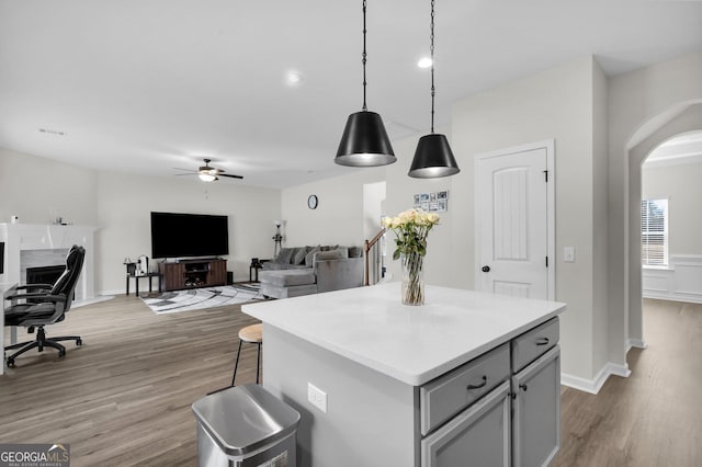 kitchen with light wood-type flooring, gray cabinetry, ceiling fan, a center island, and hanging light fixtures