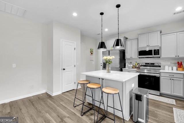 kitchen featuring appliances with stainless steel finishes, light hardwood / wood-style flooring, a kitchen island, and pendant lighting