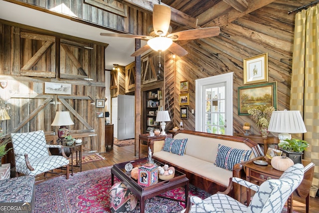 living room featuring ceiling fan, beam ceiling, wood-type flooring, and wooden walls