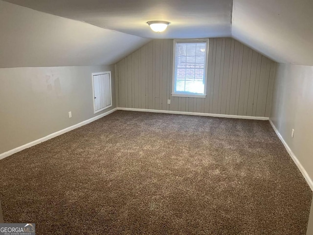 additional living space featuring carpet flooring, wooden walls, and vaulted ceiling