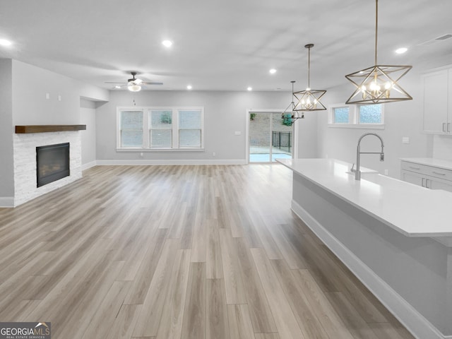 unfurnished living room with a fireplace, light hardwood / wood-style floors, ceiling fan, and sink