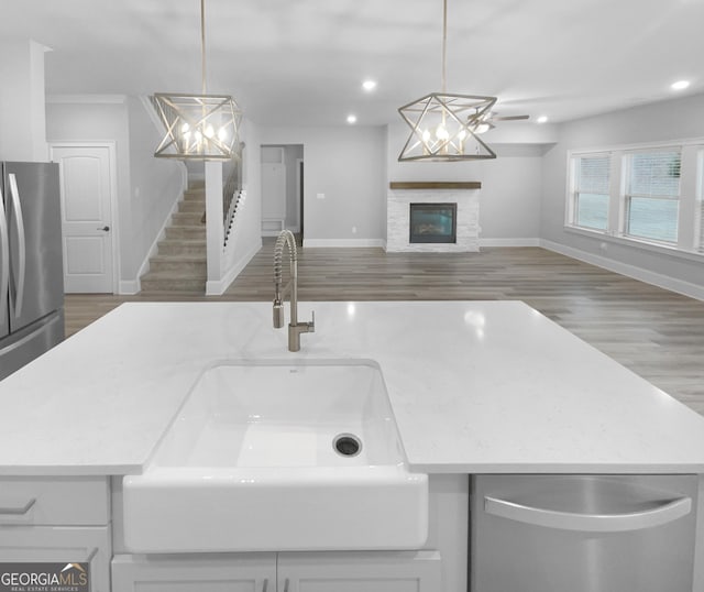 kitchen with stainless steel refrigerator, sink, hanging light fixtures, a stone fireplace, and wood-type flooring