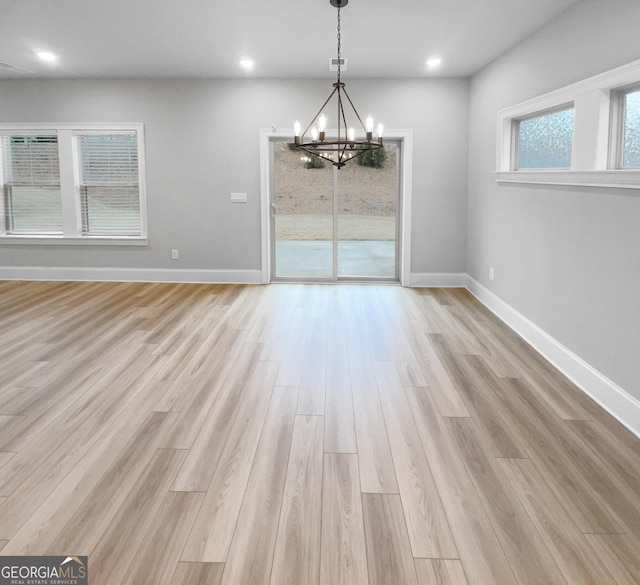 unfurnished dining area with a notable chandelier and light wood-type flooring