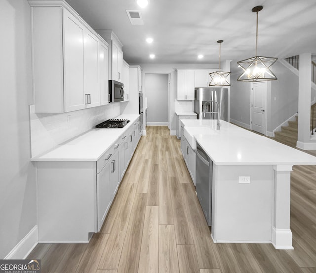 kitchen featuring white cabinetry, light hardwood / wood-style flooring, decorative light fixtures, a kitchen island with sink, and appliances with stainless steel finishes