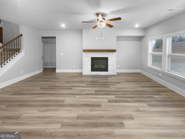 unfurnished living room featuring ceiling fan, a stone fireplace, and light wood-type flooring