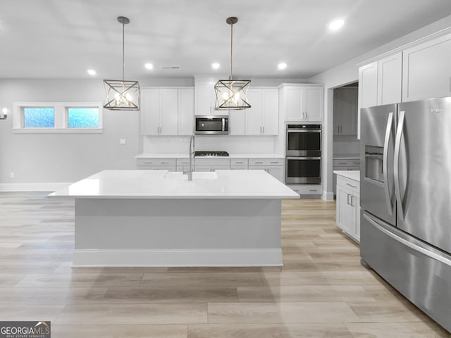 kitchen with a kitchen island with sink, white cabinets, decorative light fixtures, light hardwood / wood-style floors, and stainless steel appliances