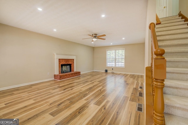 unfurnished living room featuring ceiling fan, a brick fireplace, and light wood-type flooring