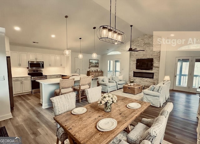dining room featuring a ceiling fan, a stone fireplace, visible vents, high vaulted ceiling, and wood finished floors