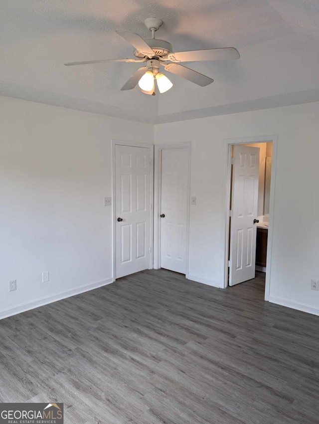 unfurnished bedroom with a textured ceiling, ensuite bath, ceiling fan, and dark wood-type flooring