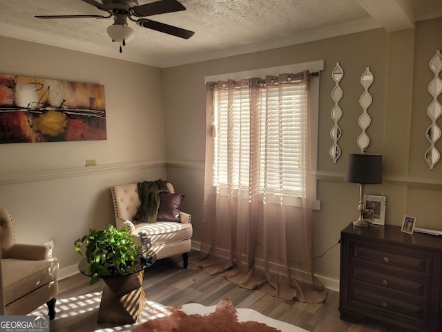 living area with ceiling fan, wood-type flooring, a textured ceiling, and ornamental molding