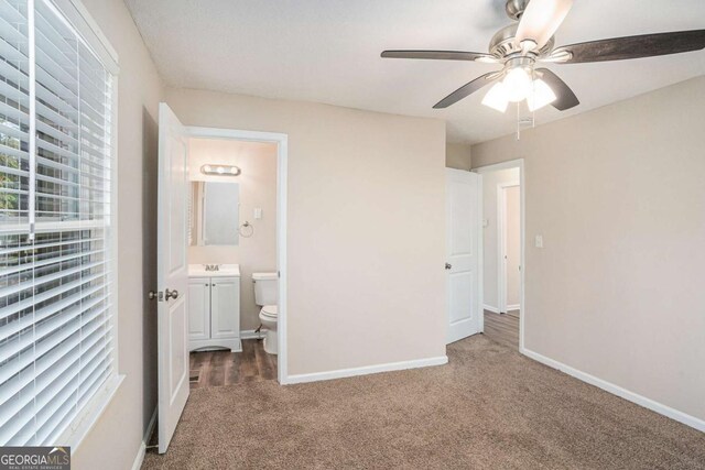 unfurnished bedroom with ensuite bath, ceiling fan, sink, and dark colored carpet