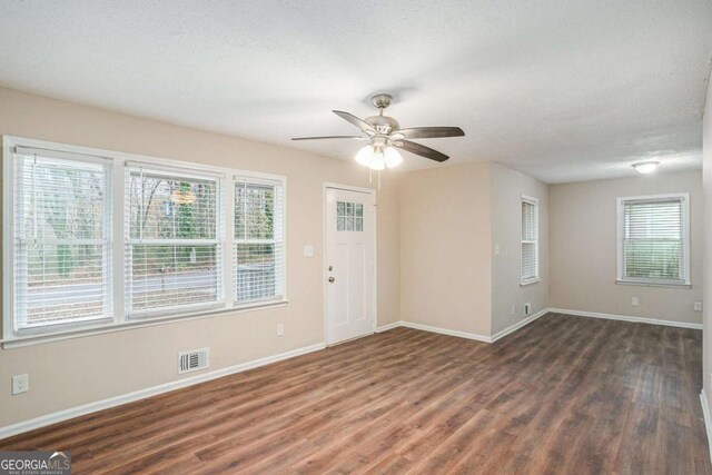 empty room featuring a textured ceiling, plenty of natural light, ceiling fan, and dark wood-type flooring