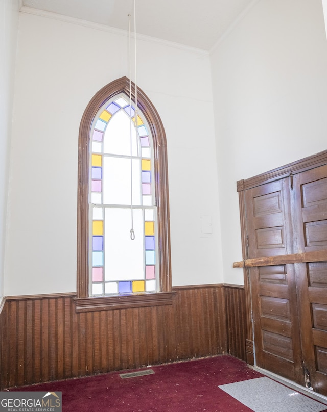 foyer entrance with carpet flooring, ornamental molding, and wood walls