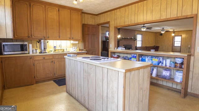 kitchen featuring a textured ceiling, ceiling fan, crown molding, white electric cooktop, and a kitchen island