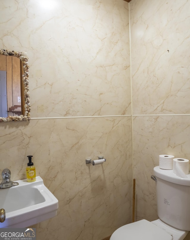 bathroom featuring toilet, tile walls, and sink