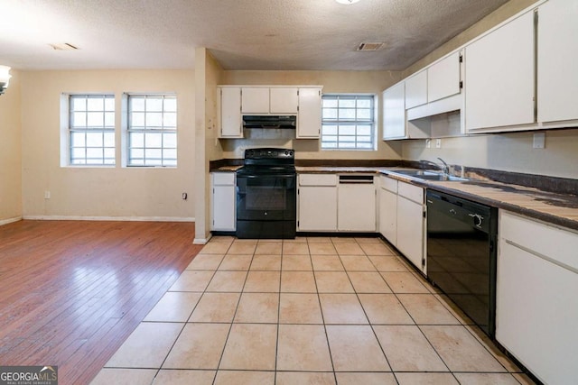 kitchen with a wealth of natural light, white cabinets, black appliances, and light wood-type flooring