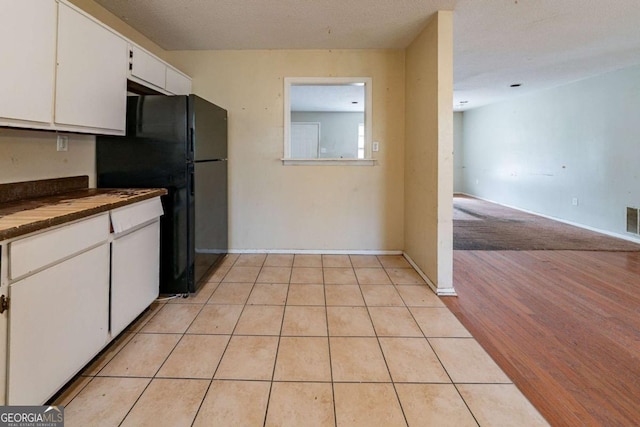 kitchen featuring white cabinetry, black refrigerator, light hardwood / wood-style floors, and a textured ceiling