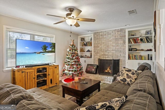 living room with a brick fireplace, a textured ceiling, ceiling fan, wood-type flooring, and built in features