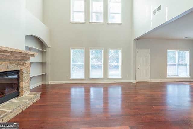 unfurnished living room with dark wood-type flooring, a stone fireplace, built in features, and a wealth of natural light