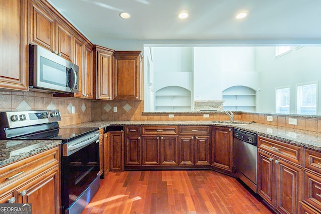 kitchen with dark wood-type flooring, sink, light stone counters, appliances with stainless steel finishes, and decorative backsplash