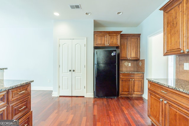 kitchen featuring light stone counters, backsplash, dark wood-type flooring, and black fridge