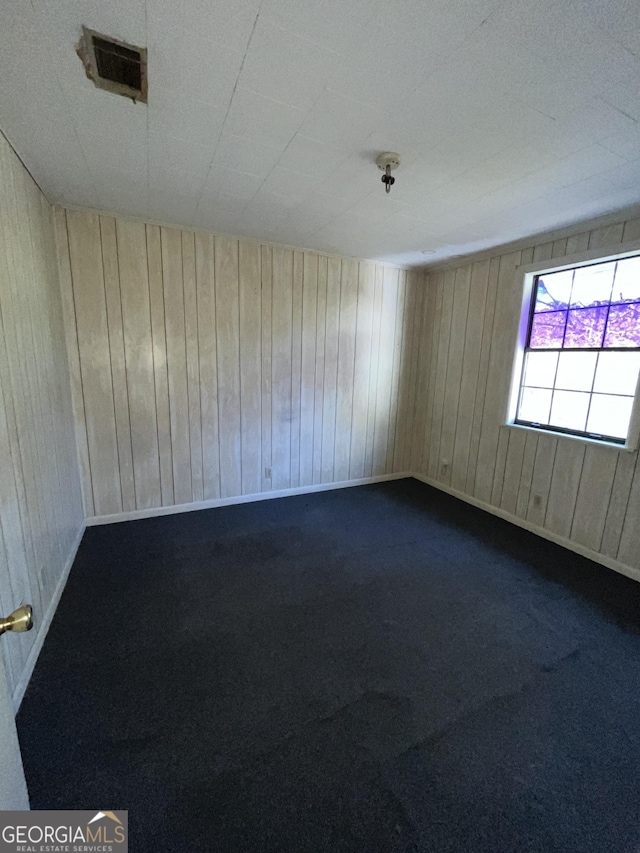 carpeted empty room featuring wooden walls