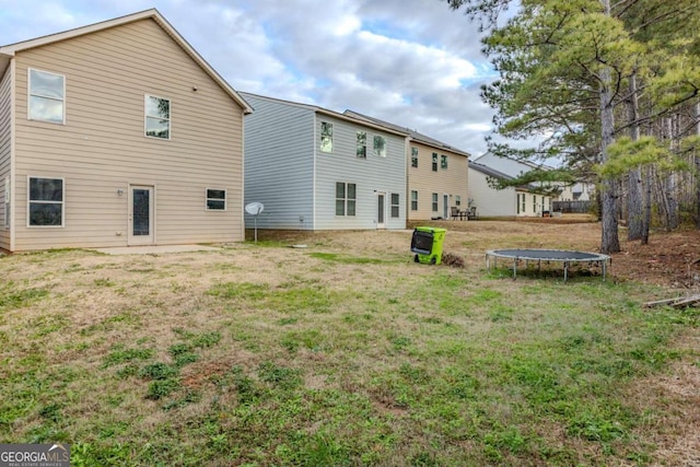 back of property with a trampoline and a yard