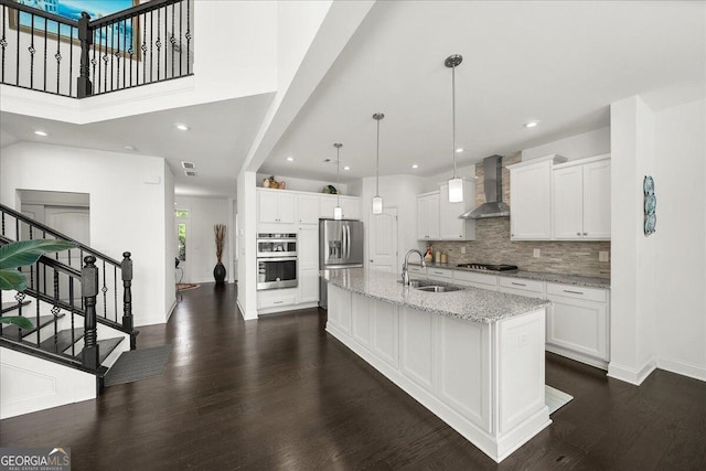 kitchen featuring sink, wall chimney exhaust hood, stainless steel appliances, an island with sink, and white cabinets