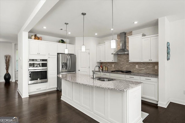 kitchen featuring sink, hanging light fixtures, wall chimney range hood, a center island with sink, and white cabinets