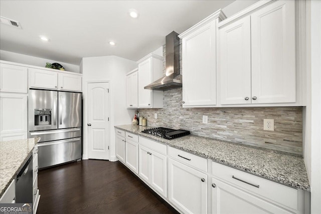 kitchen with backsplash, white cabinets, wall chimney exhaust hood, appliances with stainless steel finishes, and light stone counters