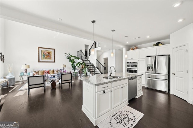 kitchen with white cabinets, hanging light fixtures, sink, an island with sink, and appliances with stainless steel finishes