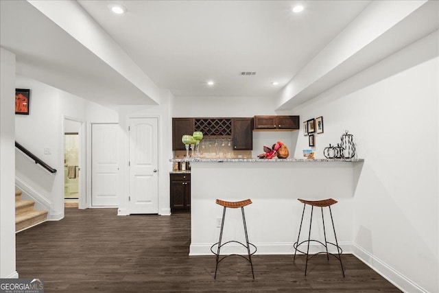 kitchen featuring light stone countertops, dark wood-type flooring, backsplash, kitchen peninsula, and a breakfast bar