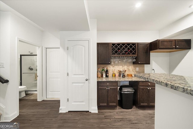 bar featuring light stone countertops, dark brown cabinetry, dark wood-type flooring, and backsplash