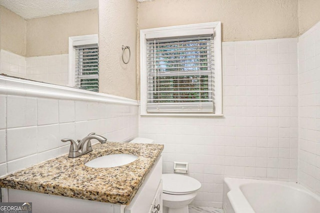 bathroom with a bathing tub, a textured ceiling, toilet, vanity, and tile walls