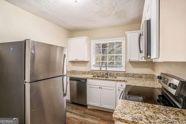 kitchen with light stone countertops, sink, stainless steel appliances, hardwood / wood-style floors, and white cabinets