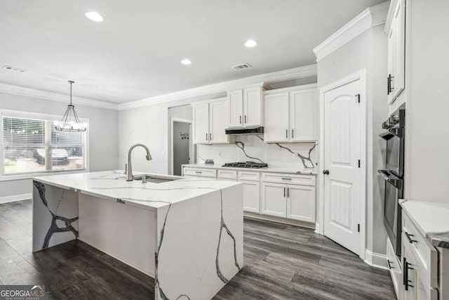 kitchen featuring a center island with sink, sink, light stone counters, white cabinetry, and stainless steel gas cooktop