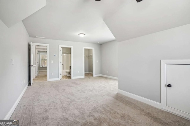 unfurnished bedroom featuring a closet, light colored carpet, a walk in closet, and ensuite bath