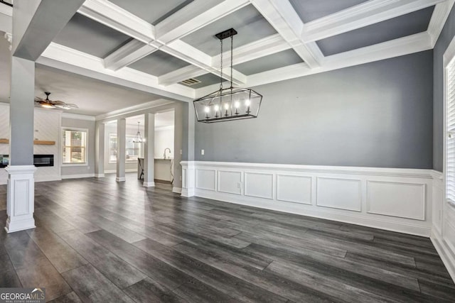 unfurnished dining area with a premium fireplace, beamed ceiling, ceiling fan with notable chandelier, and dark hardwood / wood-style floors