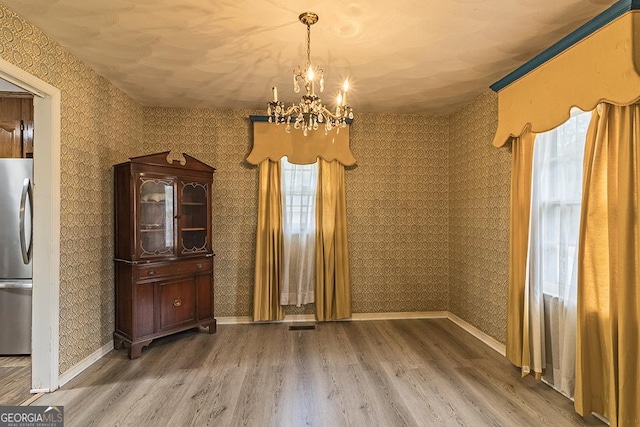 unfurnished dining area featuring wood-type flooring and a notable chandelier