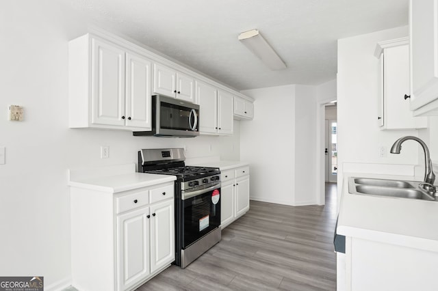 kitchen with sink, white cabinets, stainless steel appliances, and light hardwood / wood-style floors