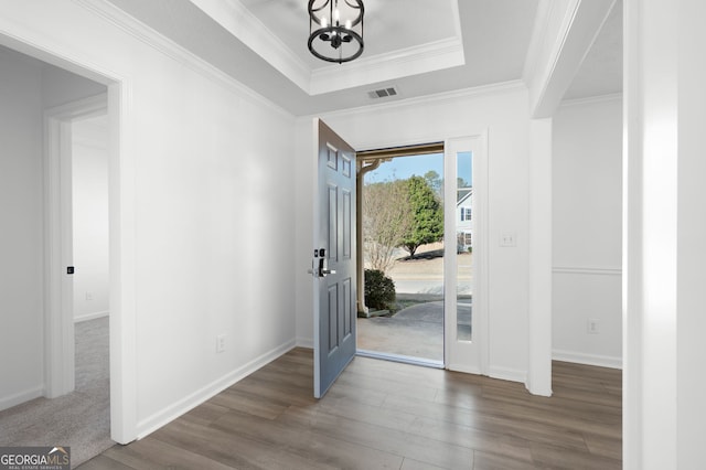 foyer entrance featuring a tray ceiling, ornamental molding, an inviting chandelier, and dark hardwood / wood-style floors