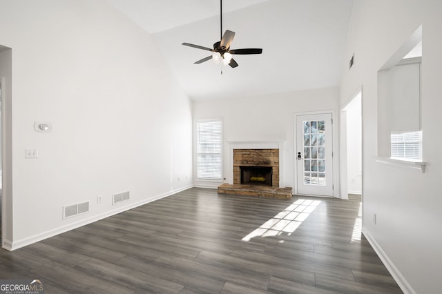 unfurnished living room with high vaulted ceiling, ceiling fan, a stone fireplace, and dark hardwood / wood-style floors