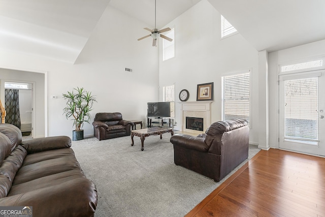 living room with ceiling fan, hardwood / wood-style floors, a towering ceiling, and a healthy amount of sunlight